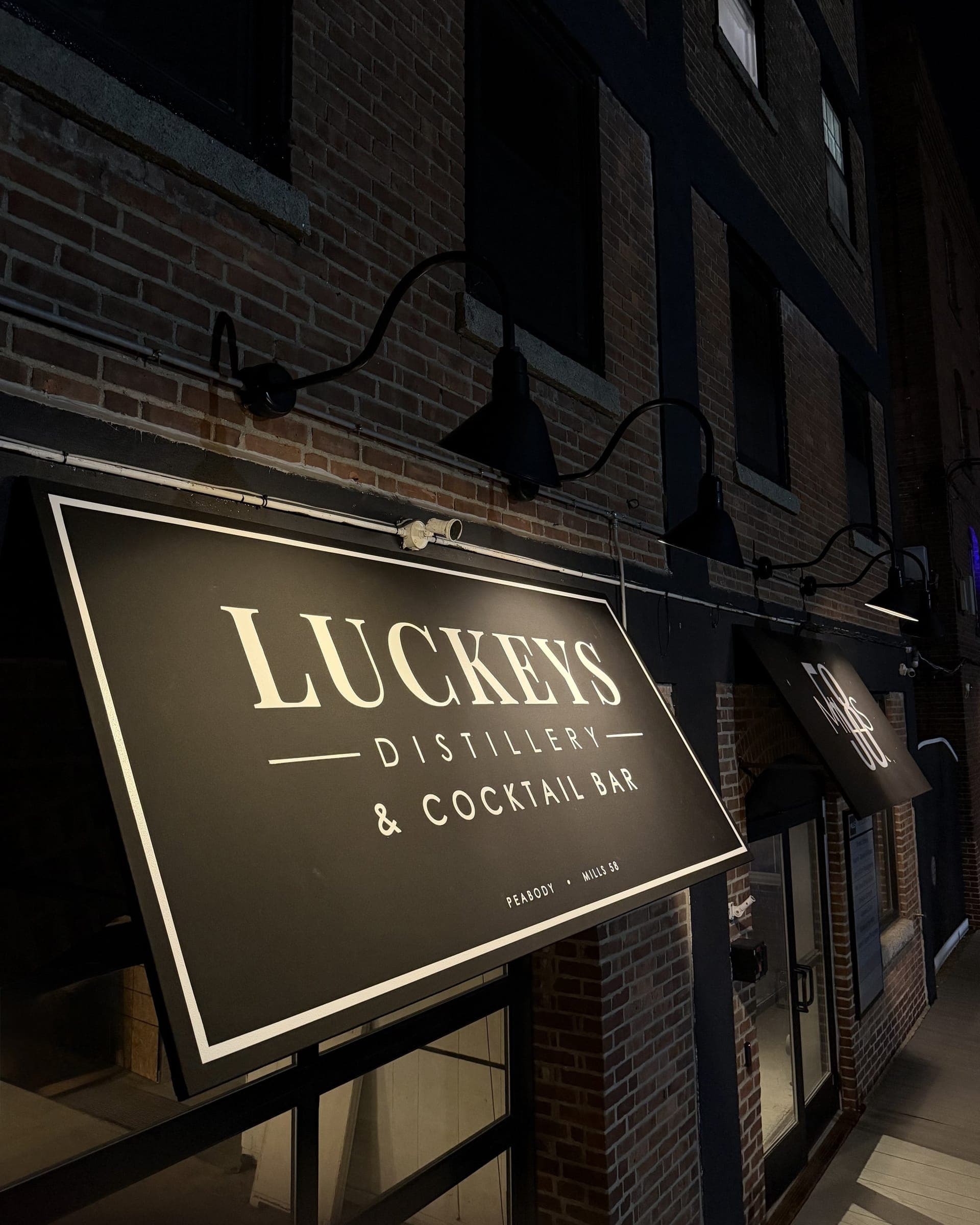 The Luckeys Distillery & Cocktail Bar sign at night, lit against the brick