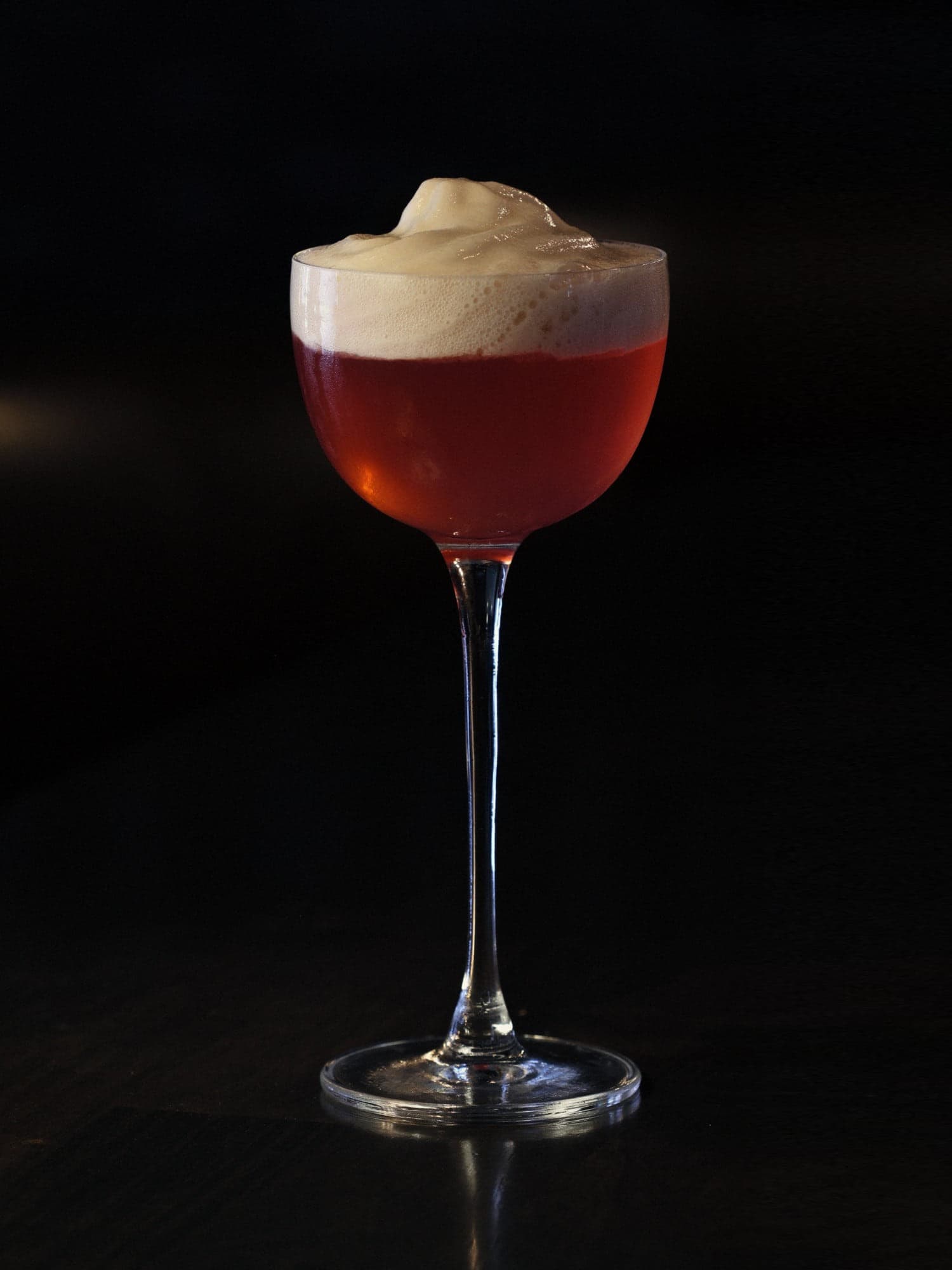 Luckeys New England Vodka, cranberry-bay cordial and lime under a chai foam — deep garnet in a tall-stemmed coupe against the dark of the bar