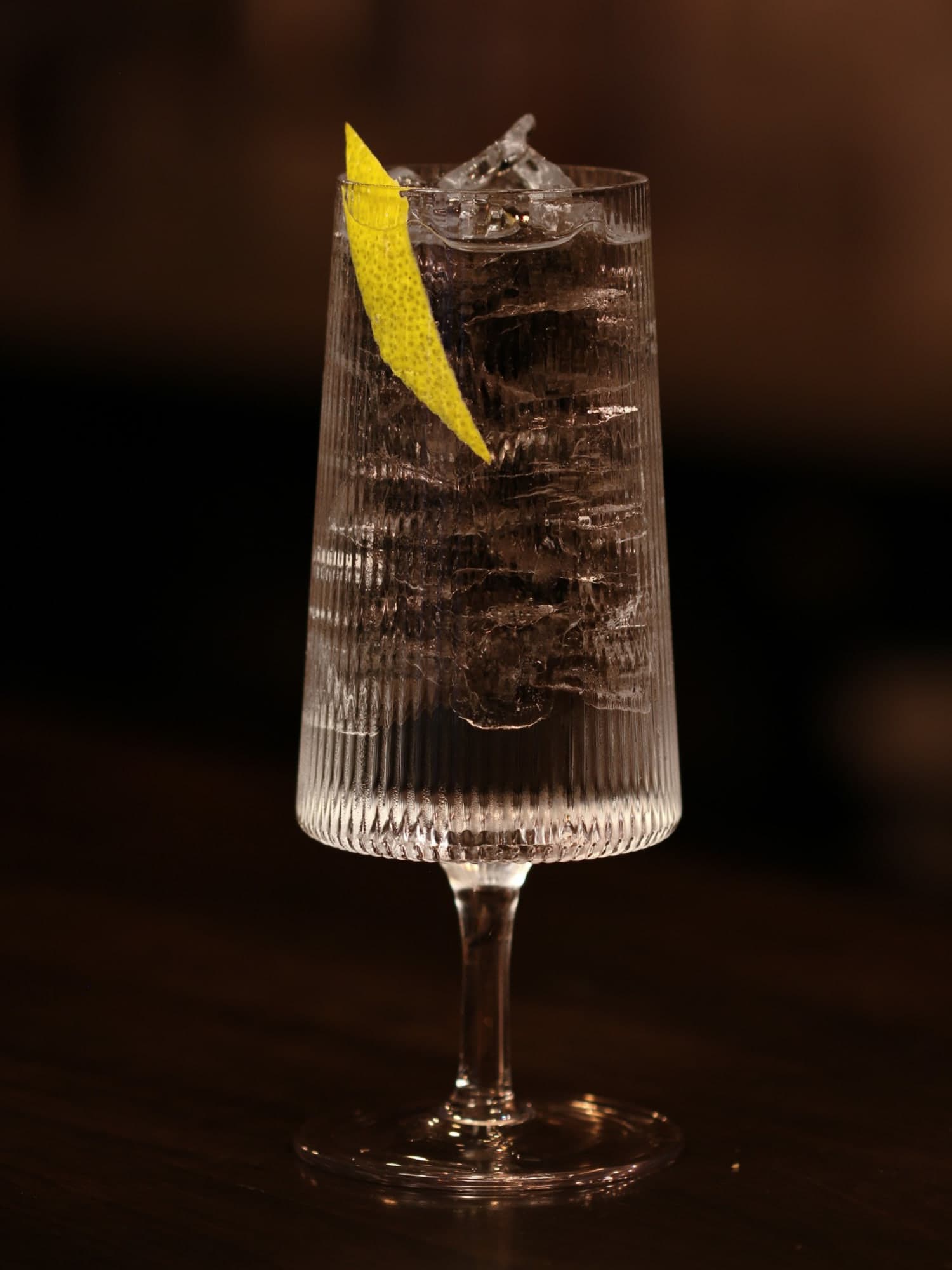 Luckeys London Dry and tonic over ice in a ribbed stemmed glass with a lemon peel, on the dark bar