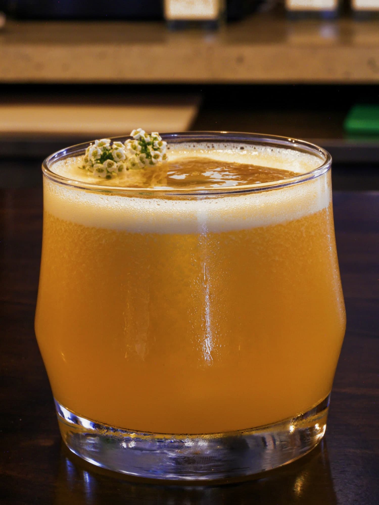 Luckeys New England Vodka, passionfruit and vanilla — golden and cloudy under a fine foam in a rocks glass on the bar, a sprig of tiny white flowers on top