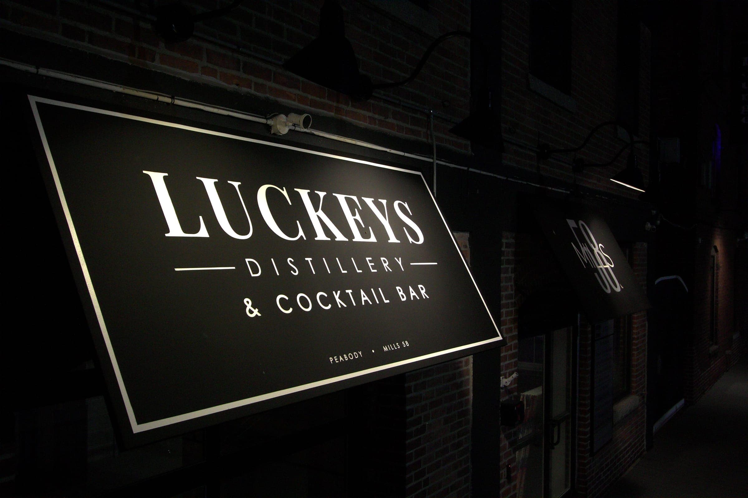 The Luckeys Distillery & Cocktail Bar sign lit over the entrance at Mills 58, Peabody, at night