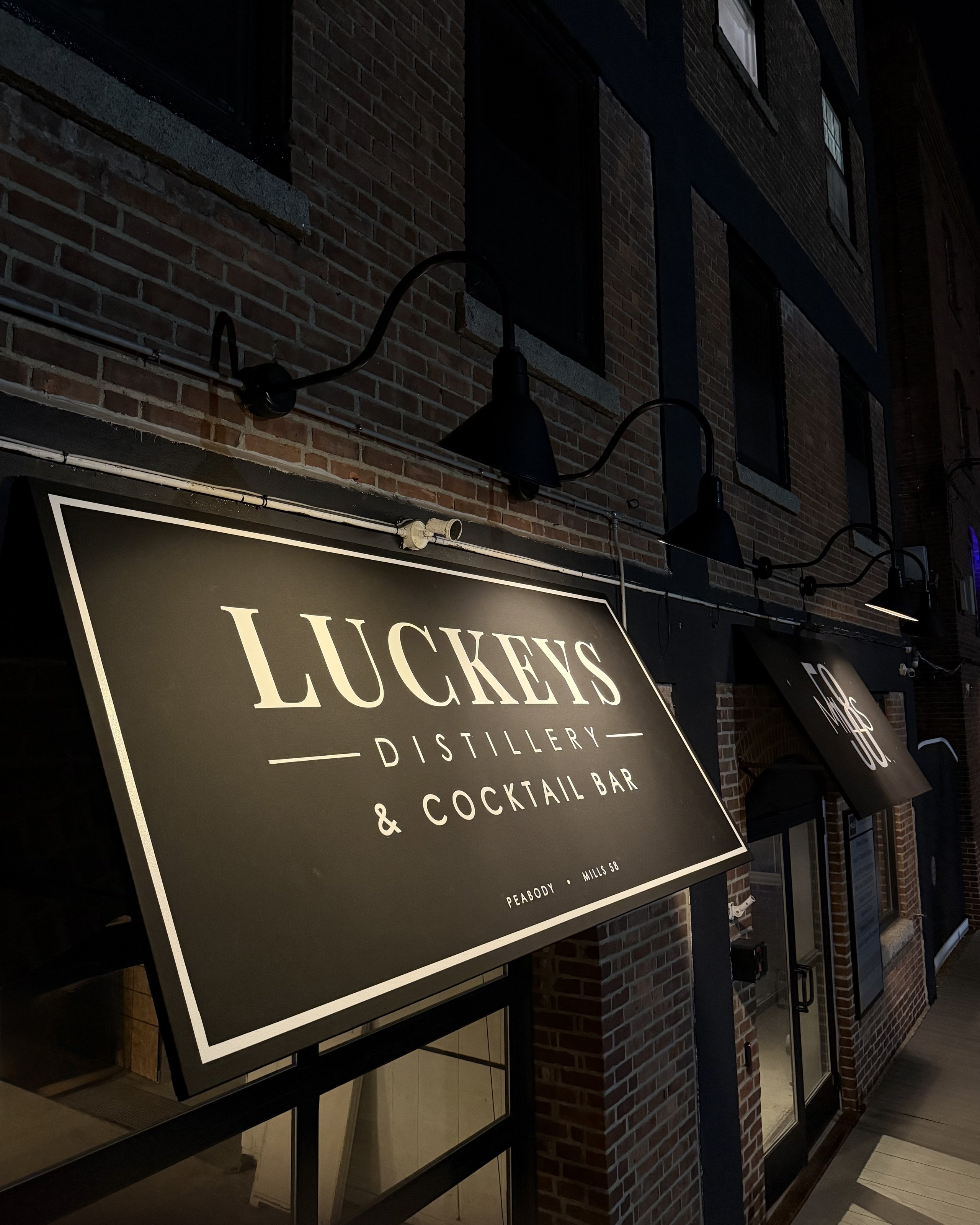 The Luckeys Distillery & Cocktail Bar sign at night, lit against the brick