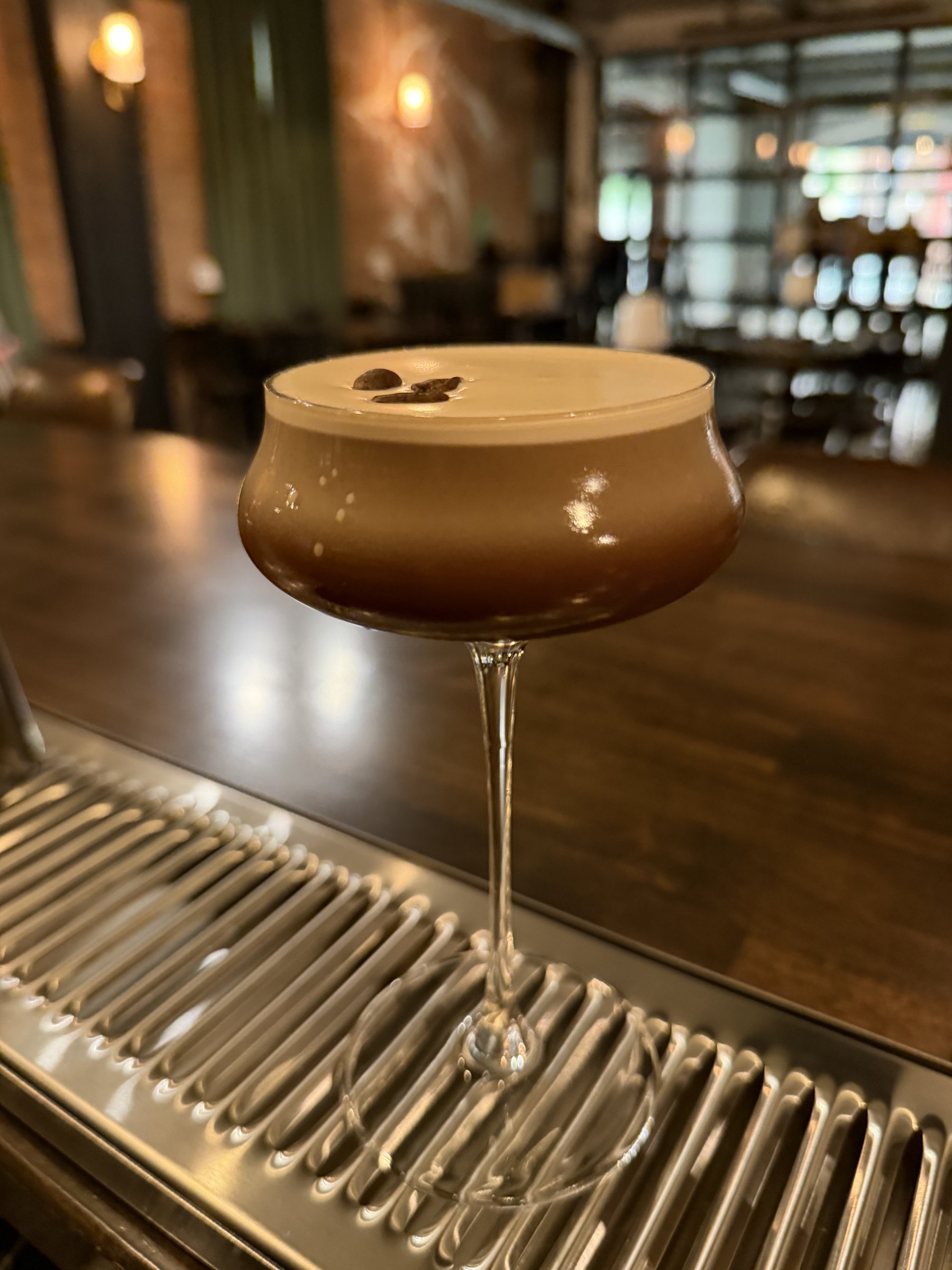 An espresso martini on the bar, the distillery glass wall behind